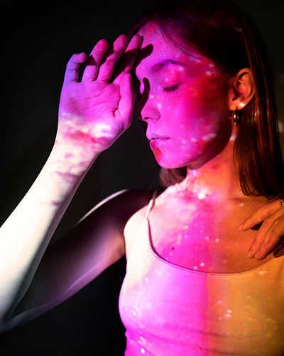 mujer con mano en rostro iluminada con luz rosa y naranja con emociones liberadas en sesion biodescodificacion