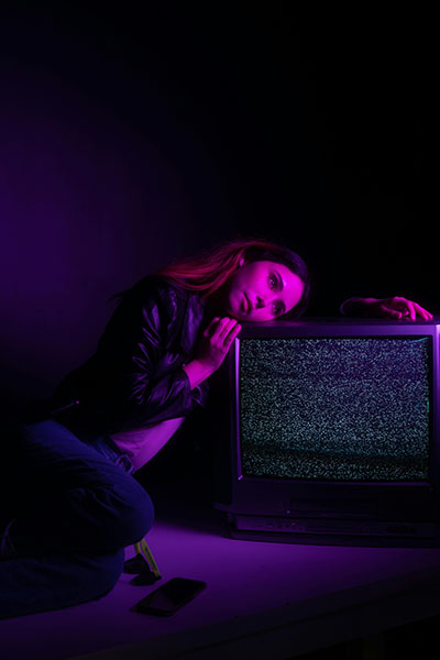chica iluminada luz de neon violeta sobre televisor cansada por mentiras que repiten biodescodificacion