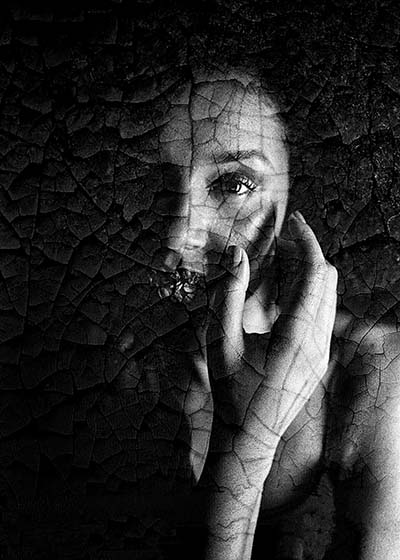 foto blanco y negro con efecto agrietado con mujer que se tapa con la mano significado biodescodificacion crisis de ansiedad
